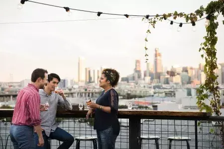 Three people gather around an outdoor table on the roof deck of Anchor Distilling in San Francisco, california.